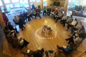 A large group of women sitting in a circle of chairs with a ring of tea lights in the center.